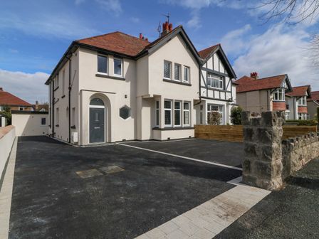 A semi detached house with a driveway and stone wall at Park View in Llandudno