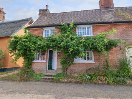 A brick cottage with climbing plants around windows and door at Brook Cottage in Peasenhall
