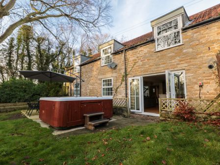 A stone house with an open patio door a hot tub and outdoor seating in a garden at The Coach House in East Ayton