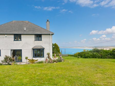 A house with a gray roof and blue window frames next to a large grassy lawn with a view of the sea at Lanyon in Carbis Bay