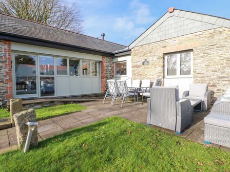 A paved patio area with outdoor dining table and chairs and wicker seating outside a stone building at The Stables in Davidstow near Camelford