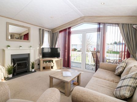 A living room with a fireplace TV sofa coffee table and glass doors leading outside at Snape Lodge Towyn