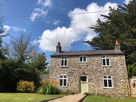 A stone cottage with a green door and white framed windows with a garden and flowers at Norden Cottage in Osmington