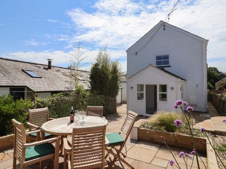 An outdoor patio with a wooden table and chairs with a bottle and glasses by a white two-story house at Backlands Farmhouse in Charmouth