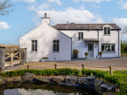 A white two-story house with a gravel driveway and plants near a small pond at Gate House in Killington near Sedbergh