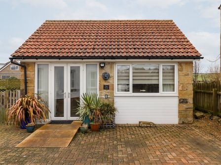 A single story building with a tiled roof two white doors and windows with plants in pots at The Nook in North Sunderland near Seahouses