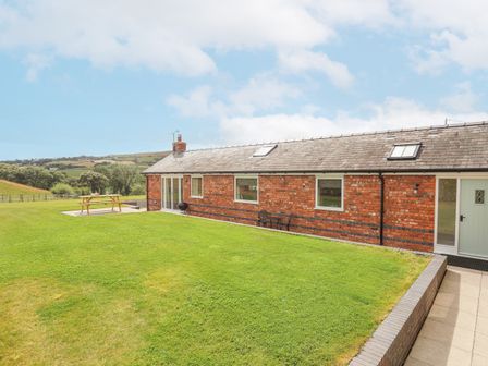 A brick house with a lawn and outdoor seating including a picnic table and a small table with chairs at The Piggery in LLanfair Talhaiarn near Abergele