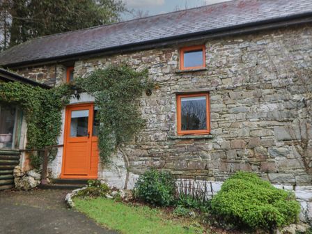 A stone house with orange door and window frames and plants growing near entrance at Ty Ceffylau in Llanllwni near Llanybydder