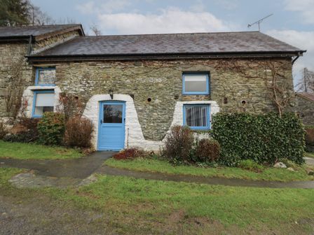 A stone building with blue door and windows surrounded by grass and bushes at Y Beudy in Cwmiar near Llanybydder
