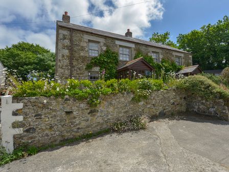 A stone cottage with a garden and stone wall under a blue sky at Swallow Cottage in Mawgan