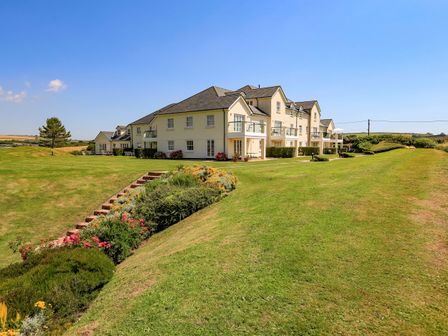 A large house with multiple balconies surrounded by a grassy lawn and flower bushes at 5 Thurlestone Beach in Thurlestone