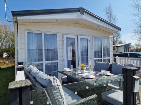 An outdoor patio area with wicker furniture and glass table set with dishes outside a small building at Ladybird Lodge South Lakes Leisure Park near Carnforth