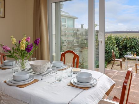 A dining table with plates glasses and a vase of flowers near a sliding glass door opening to a garden with chairs and a small table at Awalek Cumber Close in Malborough