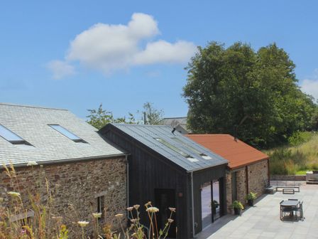A stone building with skylights and metal roofs next to a paved patio with a table and chairs at The Barns @ Downton in Dittisham