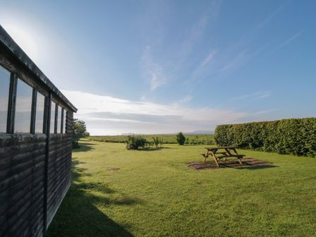 A grassy yard with a wooden picnic table near a hedge and a wooden building on the left side at Garden Cottage in Scalby
