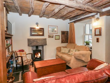 A living room with wooden beams on the ceiling a fireplace a beige sofa a patterned armchair a red leather sofa and a wooden chest table at Eden Vale in Broughton-In-Furness