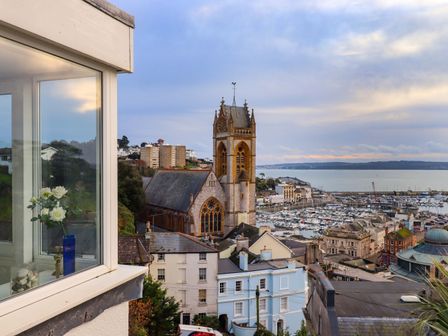A view of a church tower and buildings near a marina with boats in Torquay