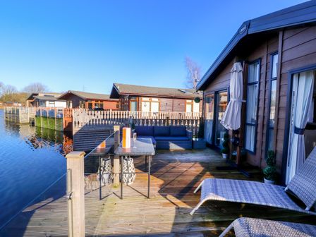 Decking area with outdoor seating and a table beside water at Gressingham 7 in Warton near Carnforth