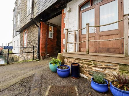 Exterior view of a building with a wooden door and multiple blue pots with plants near a water body at Zawn Nook in Falmouth