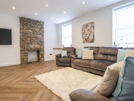 A living room with grey sofas and cushions near a stone fireplace at Gwydyr Bach 1 in Llanrwst