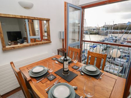 A dining table set with plates glasses and cutlery next to an open door overlooking a marina at The Sail Loft in Milford Haven