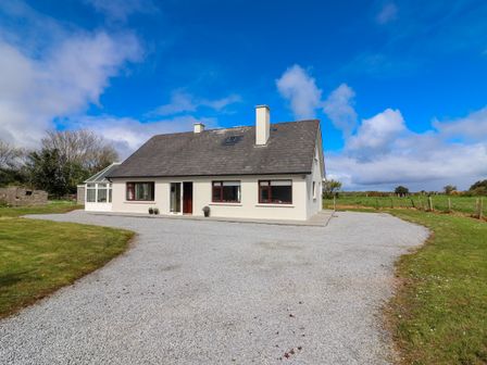A single story house with a gray roof and white walls surrounded by gravel and grass at Tonakilla House in Tonakilly near Camp County Kerry