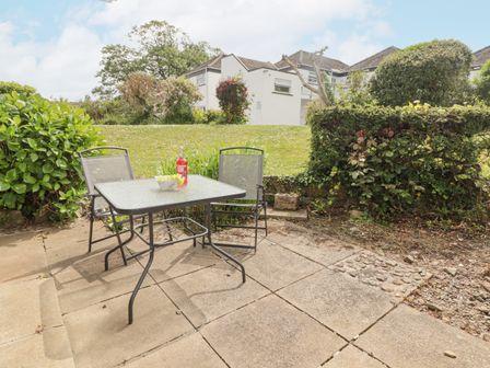 A patio with a glass table and two chairs with a bottle and a bowl on the table at 23 Coedrath Park in Saundersfoot