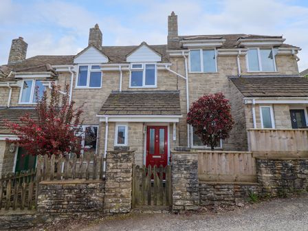 Stone terraced houses with red doors and red leafy trees behind wooden fences