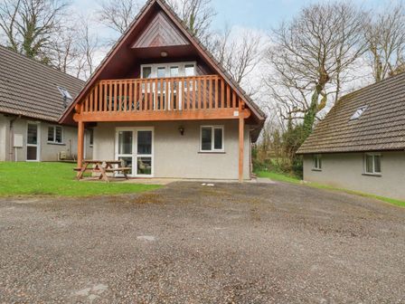 A two-story house with a balcony and picnic table in front at Rainbow Lodge in St Tudy