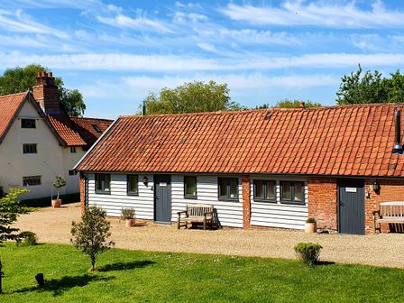An external view of a single-story building with white siding and a red-tiled roof with benches and potted plants at The Nook in Chediston near Halesworth
