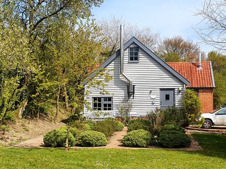 A white wooden house with a tiled roof surrounded by bushes and trees and a white car parked on the side at Twosome in Chediston near Halesworth