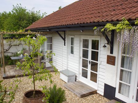 Exterior view of a white wooden building with a gravel yard a potted tree and outdoor seating at The Apple Shed in Upexe near Silverton