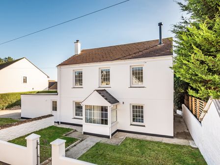 A two-story white house with a front porch and a small lawn surrounded by a low wall at Fair View in St Just in Roseland near St Mawes