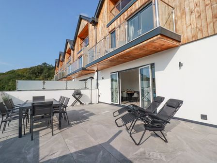 An outdoor terrace with a dining table and chairs a small grill and two reclining chairs at Carnon Gwel Devoran