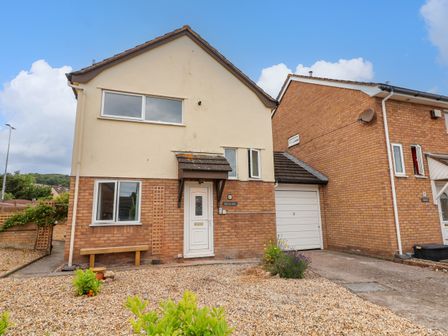 A two-story house with a gravel front yard a bench and attached garage at Carisbrook in Llandudno