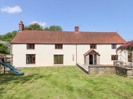 A house with red roof tiles white walls multiple windows and a green slide in the grass yard at Nempnett Farmhouse Nempnett Thrubwell near Blagdon