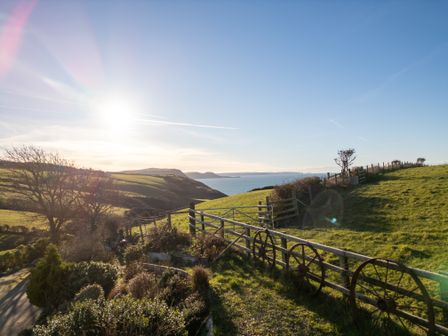 A grassy landscape with a wooden fence and old wagon wheels overlooking the sea at Crogal Stable in New Quay