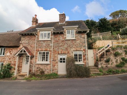 A stone cottage with two chimneys and cream painted doors and windows beside a road at Stag Cottage in Porlock