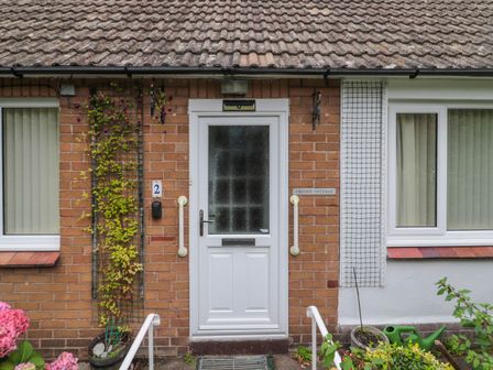 A front door with handrails and climbing plants on a brick wall at Crosby Cottage in Wooler