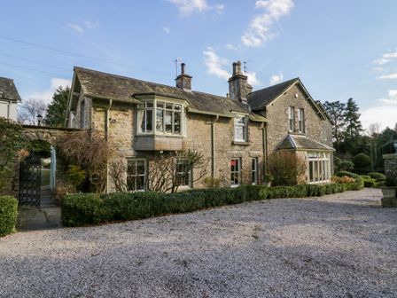 A stone house with a gravel driveway and trimmed bushes at Summerhow Retreat in Kendal