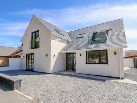 A modern white house with a slate roof a gravel driveway and a glass balcony at Blackrock Gem in Morfa Bychan