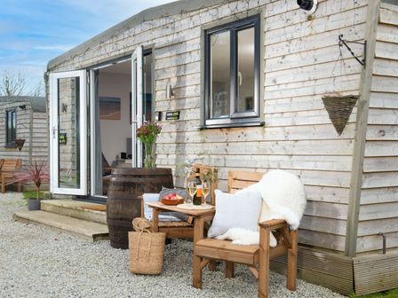 An outdoor seating area with wooden chairs and a small table with drinks outside a wooden cabin at Wheal Jewel Lodge in Wendron near Helston