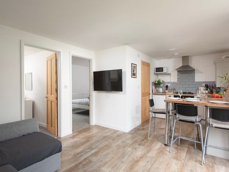 An open living and kitchen area with a wall-mounted television wooden doors and a breakfast bar with chairs at Wheal Prosper Lodge in Wendron near Helston