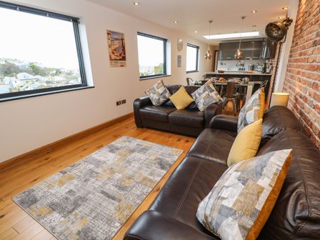 A living room with two brown leather sofas and a patterned rug next to a kitchen and dining area at Rooftops in St Ives