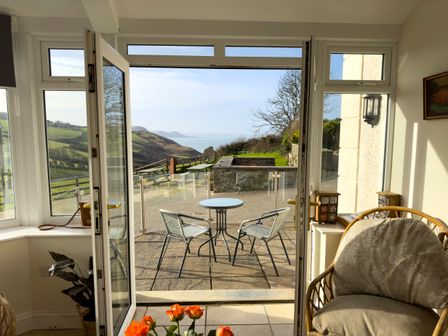 A patio with two metal chairs and a round table overlooking hills and water at Crogal Farmhouse in New Quay
