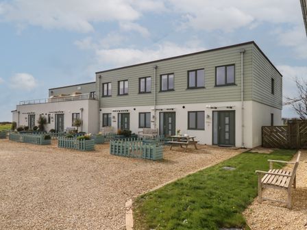 A row of modern two-story houses with green and white exterior walls and numbered doors with outdoor benches and picnic table at 5 Ocean Reach in Bolberry