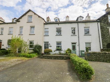 The front of a white terraced house with a driveway and garden at Acorn Cottage in Windermere