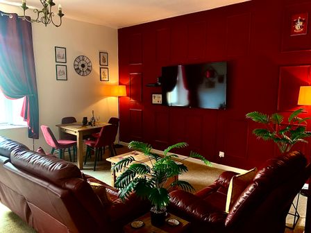 A living room with leather sofas a wooden dining table and chairs a wall mounted TV and plants at The Wizard's Chamber in Alnwick