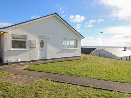 A white house with grass lawn and a concrete walkway near the ocean at Sea's The Dream in Ballinglanna near Clonakilty County Cork