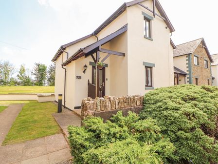 A cream colored house with a brown door a stone wall green bushes and a paved pathway at Squirrel Cottage in Penruddock